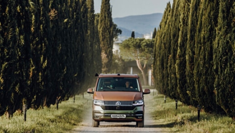 roadsurfer camper van driving down a road lined with trees in Italy