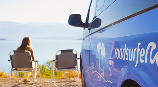 Girl sitting next to a VW camper standing at a lakeside
