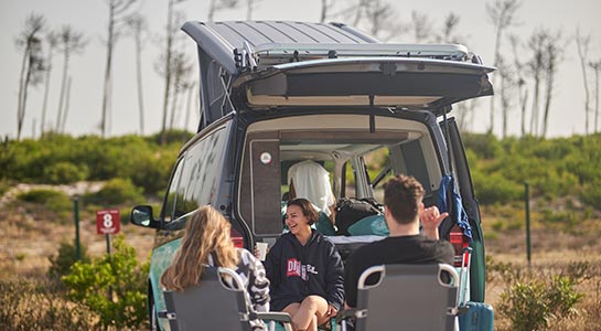 Campers at campsite, sitting outside their camper van in chairs, laughing
