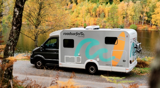 Camper van parked beside a scenic lake, surrounded by autumn-colored trees