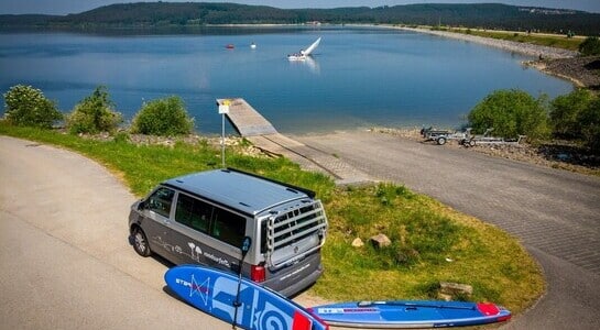 VW campervan standing in front of a lake with a wakepark.