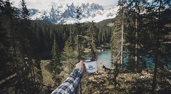 coffee spilling from a roadsurfer cup with lake and forest in the background