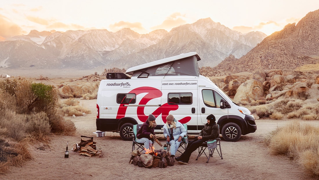 Group of friend having a good time around a campfire in the desert with campervan parked in background