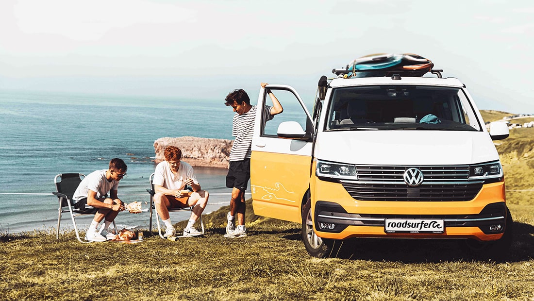Group of friends next to a VW California Beach parked on a cliff