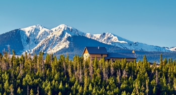 Yellow house visible through forest trees in front of the Rocky Mountains.
