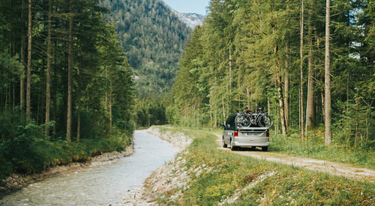 roadsurfer campervan with a bike rack driving on a small road next to a forest and a river