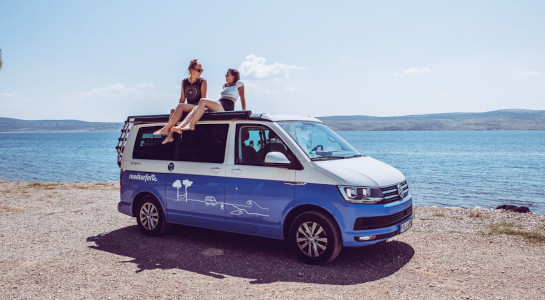 Happy girls sitting on a campervan in summer