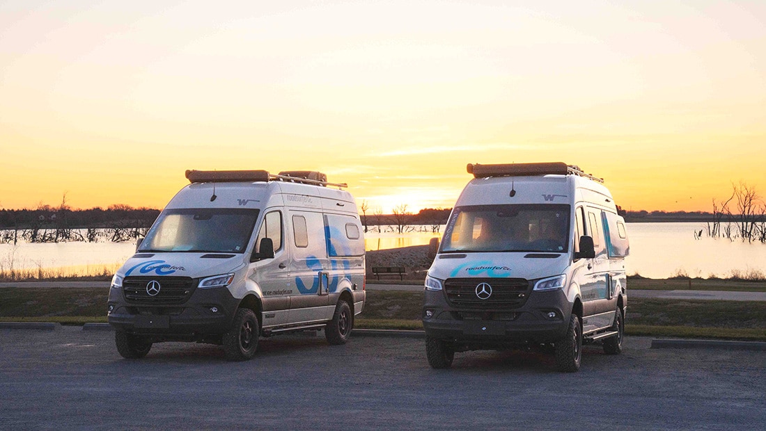 Two campervans parked by a lake at sunset
