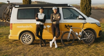 two friends with a bike posing in front of a yellow campervan