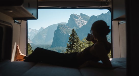 Woman relaxing in the back of a campervan looking at the mountains in the background.