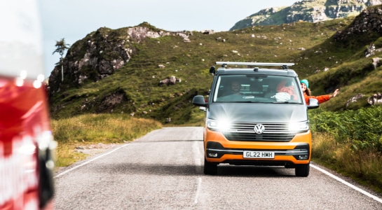 yellow campervan on a road, mountains in the background